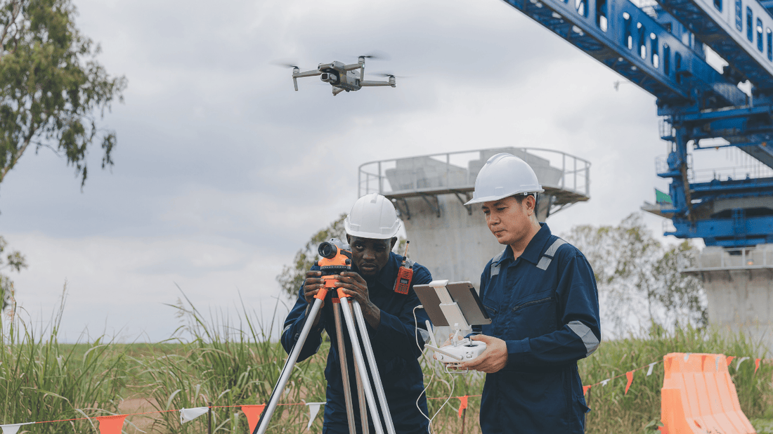 Two construction professionals operating a drone and surveying equipment on a job site to capture aerial footage and monitor project progress.
