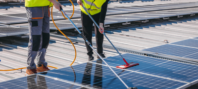 Two technicians in safety vests cleaning solar panels on a commercial roof as part of final site cleanup