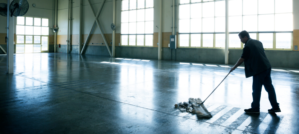 Worker mopping a large industrial warehouse floor after construction, leaving a shiny, inspection-ready finish
